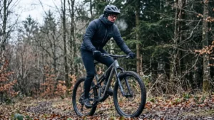 MTB odjeća za hladno vrijeme: vozač u softshell jakni i rukavicama na jesenjoj stazi kroz šumu